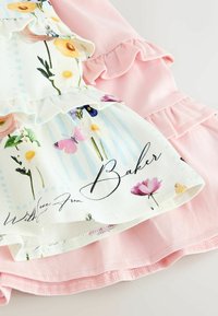 Hvidt stof med pastelblomster og sommerfugletryk lagdelt over lyserødt stof med flæsekant. Scriptt tekst delvist synlig.