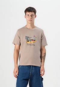Barna pamut póló, amelyen egy csontváz látható egy hajóban, mellette egy televízióval és a "JACK&JONES" felirattal alatta.