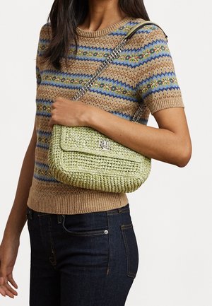 Femme portant un pull en tricot beige et bleu à motifs et un jean foncé, tenant un sac à main tissé vert clair avec une bandoulière en chaîne argentée.
