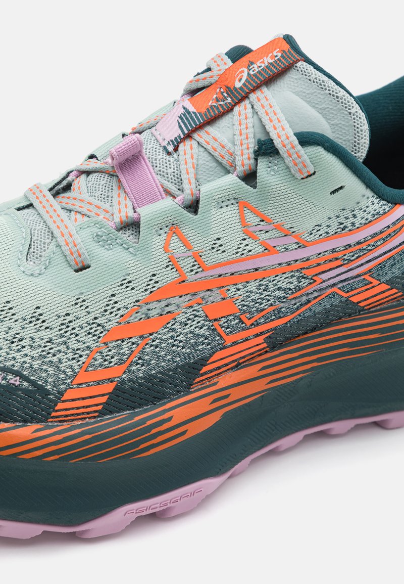 Zapatilla de correr Asics con una parte superior de malla azul claro, acentos naranjas y una suela verde texturizada. Presenta un diseño estampado y cordones rosas.