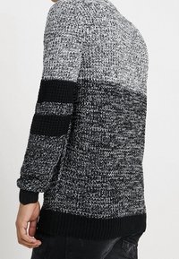 Gebreide trui met een zwart en grijs speckled patroon, met een effen zwarte manchetten en zoom. Ronde halslijn en gemiddelde dikte.