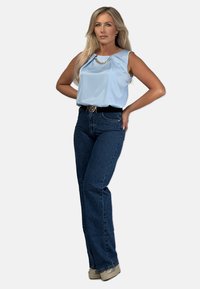 Jasnoniebieska bluzka bez rękawów z akcentem w postaci łańcuszka, zestawiona z ciemnoniebieskimi spodniami o wysokim stanie i beżowymi butami na platformie. Prosta, dopasowana sylwetka.