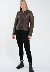 Brun læder motorcykeljakke med lynlås foran, høj krave og sidelommer med lynlås. Bæres over sorte skinny jeans og kraftige sorte støvler.