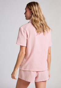 Rosa bomullspajamas med en texturerad kortärmad skjorta och matchande shorts, båda med en avslappnad passform och subtila rynkor.