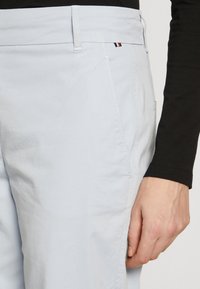 Ljust blå bomullsbyxor med en mjuk textur, utrustade med sidofickor och en liten logodetalj. Svart långärmad topp delvis synlig.