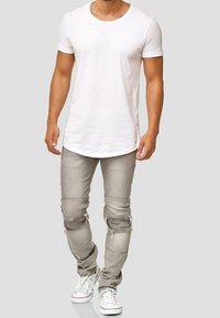 Bílé tričko s krátkými rukávy ve spojení s světle šedými džínami s roztrhanými detaily. Výrazné jsou díry na kolenou a texturované panely. Nošeno s bílými teniskami.