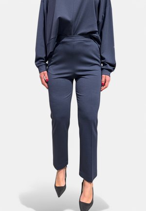 Pantaloni navy scuri realizzati in un morbido tessuto, caratterizzati da una silhouette aderente e un taglio alla caviglia, abbinati a tacchi neri a punta.