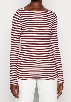 Personne portant un haut à manches longues rayé horizontal blanc et rouge foncé et un pantalon blanc, visible du cou aux hanches.