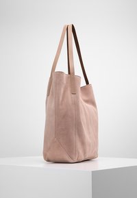 Rosa mockakviltväska med två ljusbruna läderremmar och en strukturerad, vinkelställd form. Har synlig sömnad längs sömmarna.