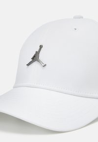 Hvid baseballkasket med en struktureret overflade. Har et sølv Jumpman-logo foran. Bøjet skygge og forstærkede syninger.