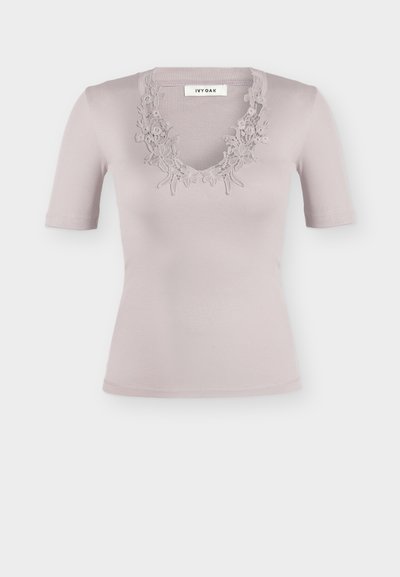 Ανοιχτό μοβ κοντομάνικο ριμπ τοπ με λουλουδάτη δαντέλα γύρω από το V-λαιμόκοψη, με ετικέτα "IVY OAK" στο γιακά.