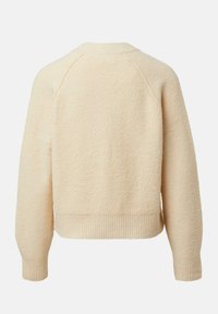 Kremowy sweter o teksturowanej powierzchni, z krótkim krojem, ściągaczem na dole i mankietach oraz rękawami raglanowymi. Miękka, puszysta tkanina bez widocznych zapięć.
