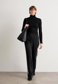 Col roulé noir et pantalon noir ample avec des rayures blanches sur les côtés, associé à un sac noir. Tissu lisse, design décontracté.