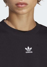Black sweatshirt with a ribbed crew neck, featuring a small white embroidered Adidas trefoil logo on the left chest area.