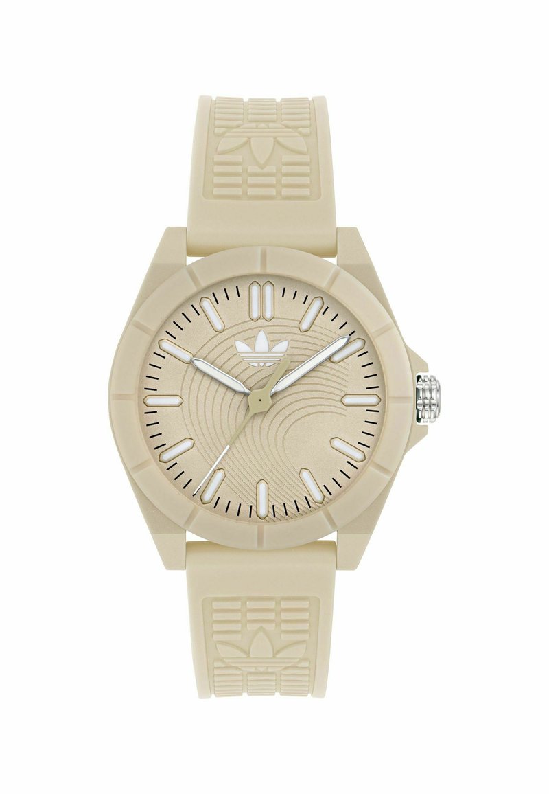 Montre en caoutchouc beige avec un bracelet texturé et un cadran rond. Elle présente des index noirs, des aiguilles argentées et un motif ondulé subtil sur le cadran.
