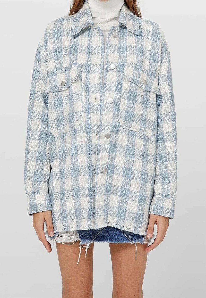 Světle modrá a bílá kostkovaná oversized bunda s límcem, druky a dvěma předními kapsami. Texturovaná látka s uvolněným střihem.