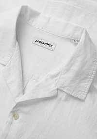 Bjela lanena košulja s kragnom, jednim gumbom na zatvaranju i JACK & JONES oznakom u crnoj boji na unutarnjoj strani kragne.