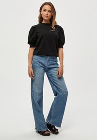 Svart topp med puffärmar, kombinerad med ljusblå vida jeans med fransar och svarta sandaler. Enkelt design och avslappnad stil.