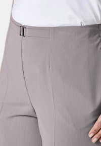 Graue, maßgeschneiderte Hose mit glatter Textur, die mit einem Taillenverschluss und dezenten Falten für einen strukturierten Sitz versehen ist. Nahaufnahme von der Seite.