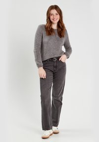 Suéter de punto gris de manga larga, combinado con jeans negros de cintura alta y zapatillas blancas con detalles en marrón. Fondo liso.
