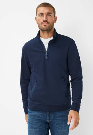 Navy Pullover aus weichem Stoff, mit einem halben Reißverschlusskragen, zwei Reißverschlusstaschen und einer sportlichen Passform mit geripptem Saum.