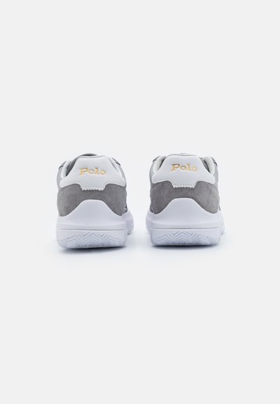 Tenisi gri și albi cu un superior din suede și plasă, având o talpă din cauciuc și logo-ul "Polo" în aur pe călcâi.
