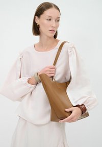 Borsa a spalla in pelle marrone con una forma strutturata, un manico lungo e un accento marrone a contrasto alla base. Texture liscia senza motivi visibili.