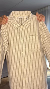 Camicia a righe con bottoni in crema e marrone chiaro, con colletto, tasca frontale e tessuto testurizzato con linee verticali.