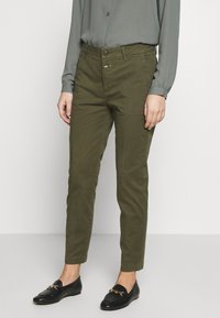 Pantalon chino vert olive à coupe ajustée, doté d'une braguette zippée, d'une fermeture par bouton, et de deux poches avant. Associé à des mocassins noirs.