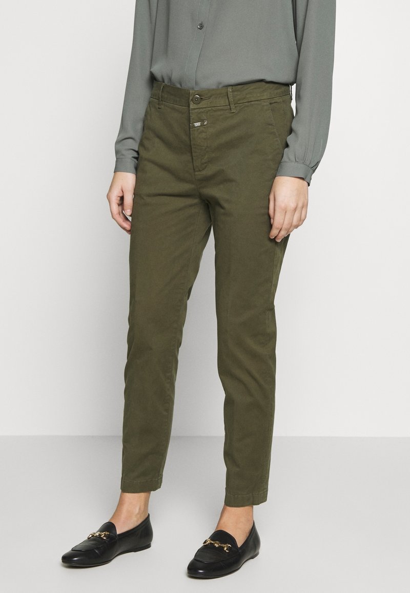 Pantalon chino vert olive à coupe ajustée, doté d'une braguette zippée, d'une fermeture par bouton, et de deux poches avant. Associé à des mocassins noirs.