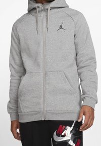 Sudadera gris con cremallera hecha de una mezcla de algodón, con un bolsillo canguro, puños acanalados y un logo Jumpman negro en el pecho.