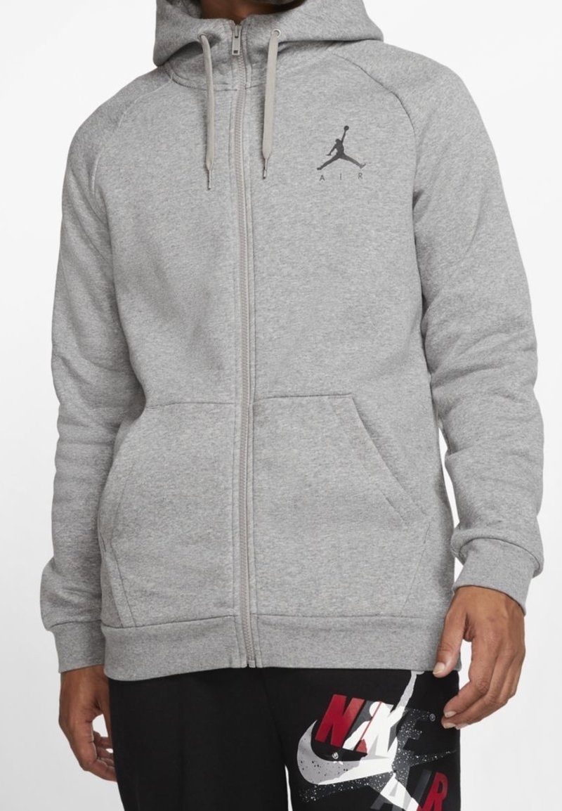 Sudadera gris con cremallera hecha de una mezcla de algodón, con un bolsillo canguro, puños acanalados y un logo Jumpman negro en el pecho.