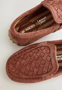Chaussures à enfiler en daim marron avec un motif matelassé, des détails cousus, et une semelle en caoutchouc texturée avec une doublure intérieure rayée.