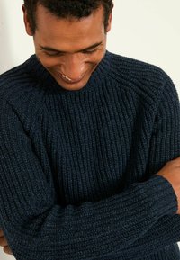 Marineblauer Strickpullover mit geripptem Muster, hochgeschlossen und mit langen Ärmeln, die an den Manschetten eng anliegen, aus der Nahaufnahme dargestellt.