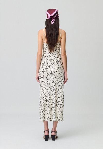 Vestido midi blanco con lunares negros, tirantes finos ajustables, ligera curva en el dobladillo, combinado con sandalias de tacón negro, modelo de espaldas.