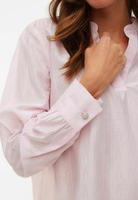 Langermet rosa bluse med strukturert stoff, utstyrt med en hakket krage og en knapp med rhinstein-dekor på mansjetten.