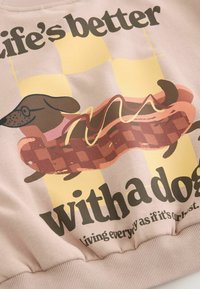 Light pink sweatshirt featuring a graphic of a dachshund on a hot dog with yellow mustard, set against a checkered background and bold text.