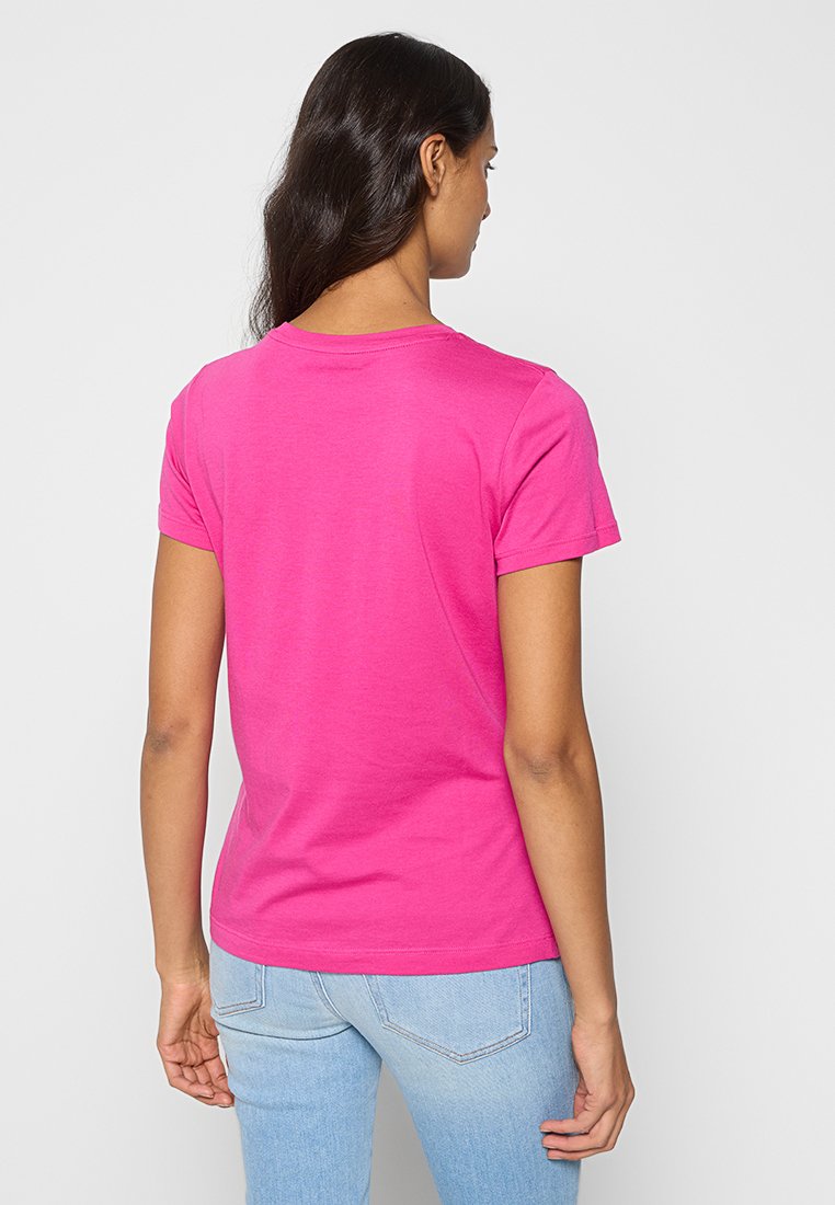Różowa bawełniana koszulka z krótkim rękawem i okrągłym dekoltem, o gładkiej fakturze. Model ma na sobie jasnoniebieskie dżinsy.