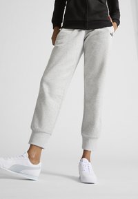 Svetle šedé fleecové tepláky s žebrovanými manžetami a bočními kapsami, doplněné bílými teniskami s jemným světle modrým akcentem.