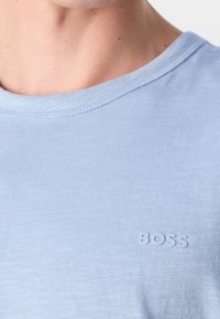 Gros plan d'une personne portant une chemise bleu clair avec le mot "BOSS" imprimé sur la poitrine près de l'encolure.