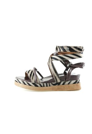 Sandał na koturnie z paskami w czarno-biały wzór zebry, ciemnobrązowe skórzane akcenty i jasnobrązowa korkowa podeszwa.