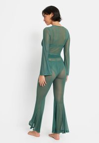 Completo in rete verde trasparente con maniche lunghe, pantaloni svasati e vita aderente. Presenta una texture sottile e dettagli in strati.
