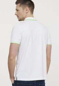 Witte poloshirt met korte mouwen en groene gestreepte accenten. Het shirt heeft een klassieke kraag en zijsplitten aan de zoom.