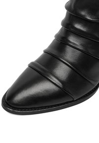 Czarny skórzany botek do kostki o spiczastym nosku, z plisowanymi detalami i gładką teksturą, osadzony na płaskiej podeszwie z przeszywanym obramowaniem.