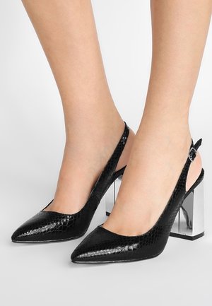 Czarne czółenka na obcasie z odkrytymi piętami, o szpiczastym nosku, z wzorem węża i masywnym metalicznym obcasem. Regulowane zapięcie na kostce.