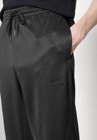 Černé sportovní kalhoty z hladké, lehké tkaniny. Mají pružný pas, boční kapsy a nenápadné logo Nike u kapsy.