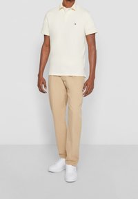 Ljusgul polo skjorta med korta ärmar, i kombination med beige byxor och vita sneakers. Har en liten logotyp på skjortans bröst.