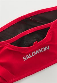 Red fabric waist pouch with a mesh interior. Features a silver "SALOMON" logo and elastic trim for secure fit. Lightweight and compact design.