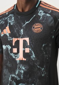 Gros plan d'un maillot de football du FC Bayern Munich noir et bleu marbré avec des logos orange et des bandes sur les épaules.