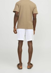 T-shirt en coton beige, shorts en lin blancs et tongs marron. La tenue a une coupe décontractée avec des manches courtes et un design simple.